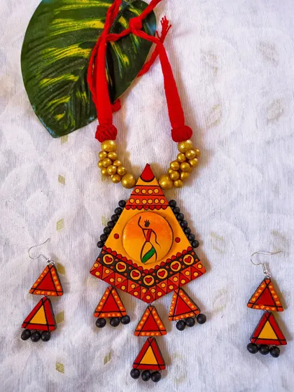 This hand-painted tribal art set features a dancer motif against a bright, sun-like background. The geometric pendant and matching earrings make it a striking piece for ethnic wear collections.