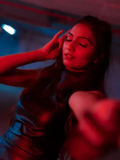A sensual and moody close-up, with the model's hand reaching towards the camera, bathed in a mix of red and blue light.