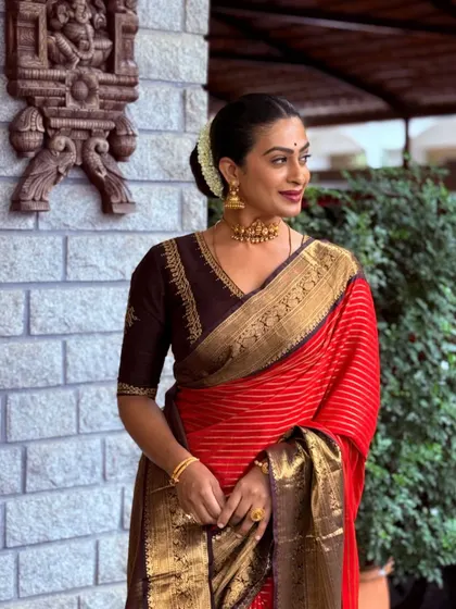 A graceful pose from a client in a deep brown raw silk blouse. The minimal embroidery along the neckline and sleeves highlights the beautiful drape of her red and gold saree.