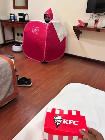 The two different worlds of a fight camp. While one fighter is in the final stages of a tough weight cut using a portable sauna, the team's support system is right there, even if it means eating KFC in the same room. This is the reality of the fight game.