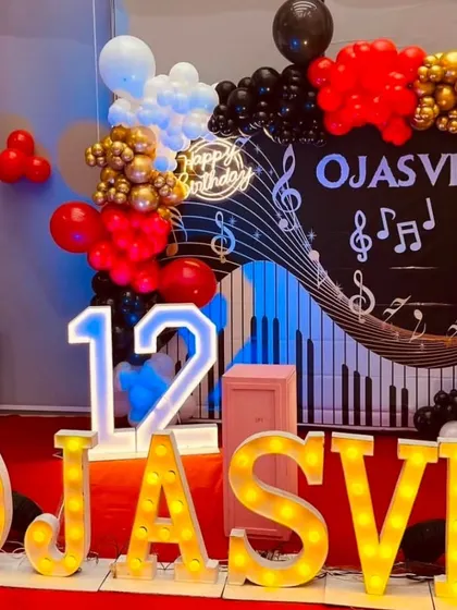 A music-themed 12th birthday party. The backdrop features a keyboard and music notes, with red, black, and gold balloons and the birthday girl's name in large marquee letters.