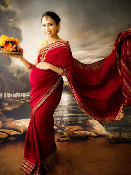 A graceful and traditional portrait. The mom-to-be, dressed in a red saree, holds a plate of marigolds, her flowing pallu adding a touch of drama.