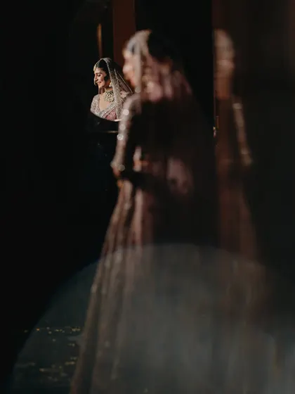 An artistic reflection shot of a bride looking in a mirror. This creative portrait captures a moment of quiet contemplation with a vintage, glamorous feel.