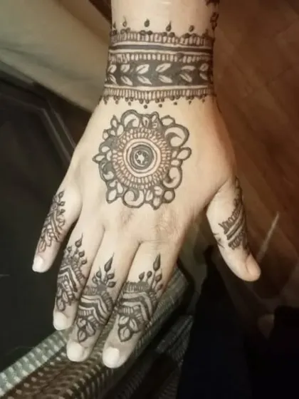 A simple mandala on the back of the hand with a leaf-patterned wristband.