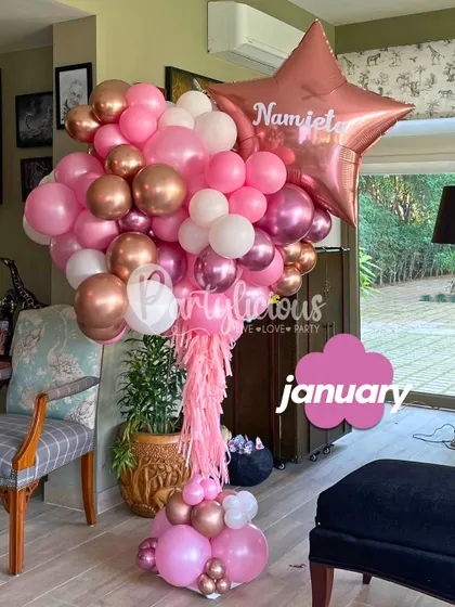 A gorgeous pink and rose gold balloon bouquet for a January birthday, personalized with the recipient's name on a star balloon.
