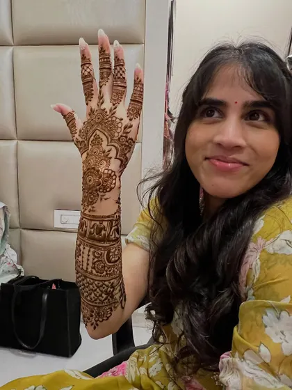 A happy bride showing off her intricate mehendi, which was carefully designed to work around her existing forearm tattoo.