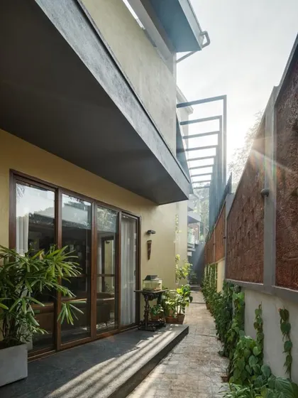 A view of the landscaped setback, where a laterite stone wall and climbing plants create a textured, living boundary. Large glass doors ensure this sliver of nature is always visually accessible from inside.