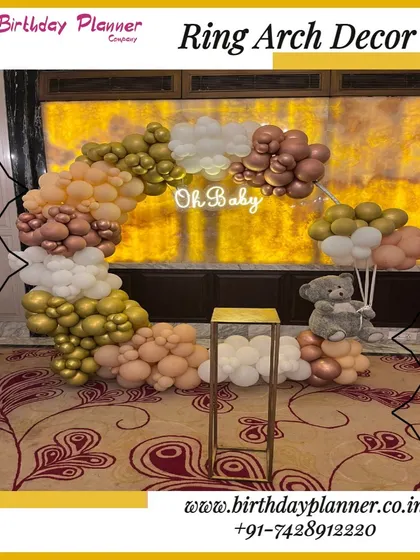 A lovely "Oh Baby" themed decoration featuring a half-ring balloon arch in gold, rose gold, and white. A small teddy bear prop adds a touch of sweetness to this baby shower photo corner.