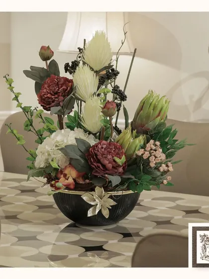 This stunning floral arrangement, with its mix of deep reds, whites, and unique artichoke blooms, creates a dramatic and sophisticated centerpiece for a modern dining table.