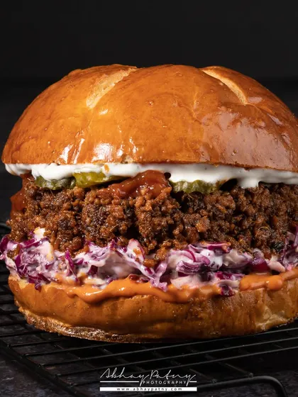 This burger shot is all about texture. The dark, close-up framing emphasizes the crunchy coating of the patty and the glossy brioche bun, creating a powerful, craving-inducing image.