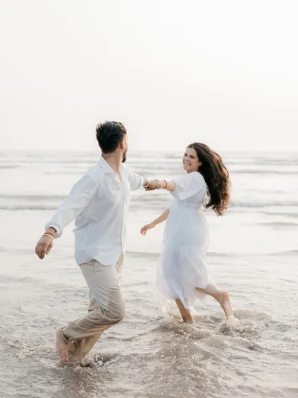 A fun, dynamic shot of a couple playing in the waves, splashing and laughing together. It shows the playful and carefree side of their relationship during their pre-wedding session.