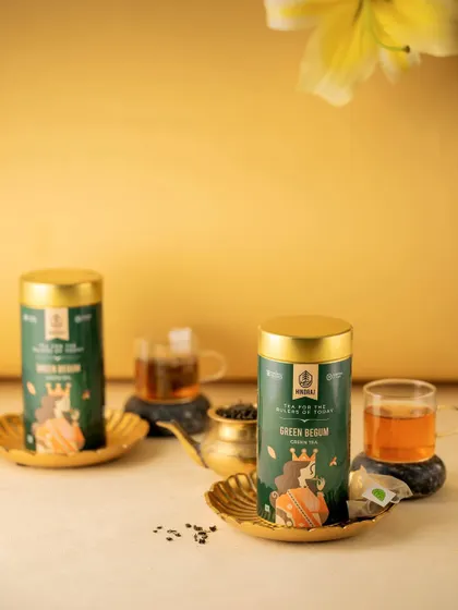 An elegant shot of Hindraj's Green Begum tea tins. The golden background and delicate lighting create a premium feel, highlighting the product's sophisticated branding.