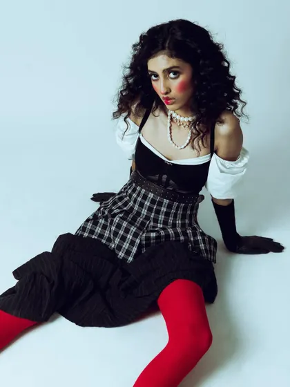 A close-up of the model in a doll-like pose. The styling and expression work together to create a distinct, memorable character for this editorial.