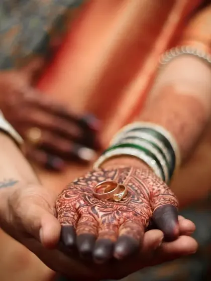 A close-up, artistic shot showing the wedding rings resting in the bride's henna-adorned palm, held gently by the groom. This detailed photograph symbolizes the promise and beginning of a new life together.