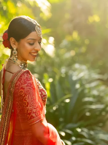 A stunning solo portrait of the bride in her red wedding lehenga, captured in the golden light of the setting sun.