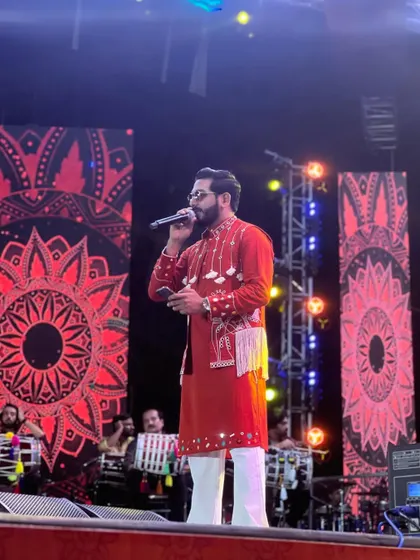 Addressing the crowd during a Navratri night. My custom red ethnic outfit stands out against the vibrant stage backdrop.