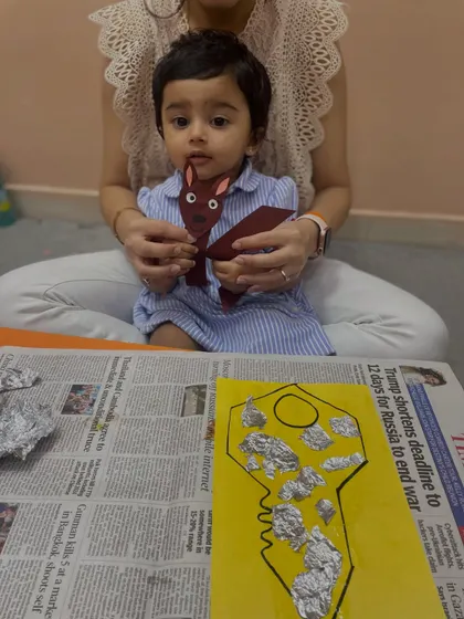 A toddler holds up a paper kangaroo craft while sitting with her mother, showcasing another animal-themed alphabet activity.