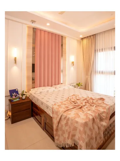 This bedroom uses a soft pink fluted headboard as a beautiful focal point. The design is warm and inviting, with elegant lighting and rich wooden furniture.