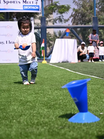 An Independent Toddler Program student carries a ball in a scoop, practicing her balance and coordination.