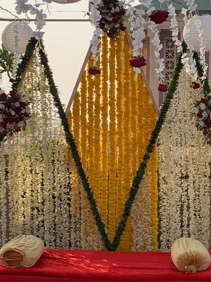 A unique Haldi setup with a triangular backdrop made of marigold and tuberose flower strings, creating a modern yet traditional look.