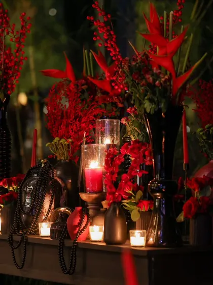 An arrangement of red florals in black vases, illuminated by candlelight. The interplay of shadow and light creates a moody and sophisticated ambiance.