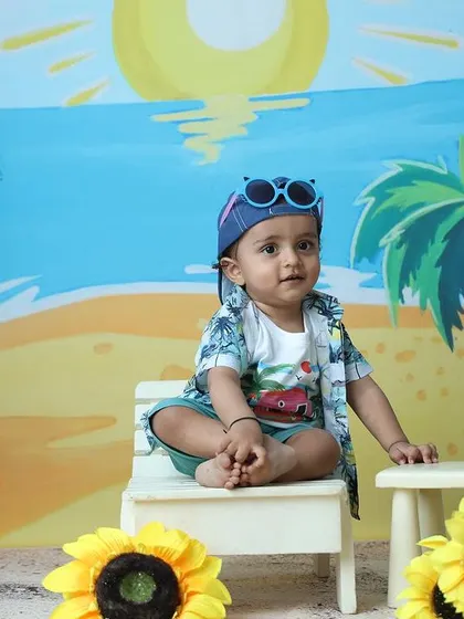 The toddler poses with sunglasses perched on his cap, showing off his cool beach attire.