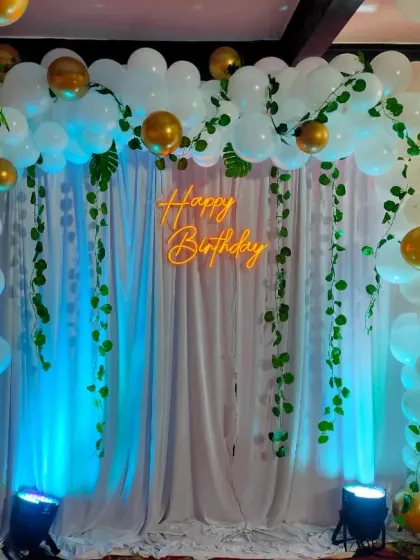 A clear, straight-on view of the elegant white, gold, and greenery balloon arch with the neon sign, perfect for first birthdays.