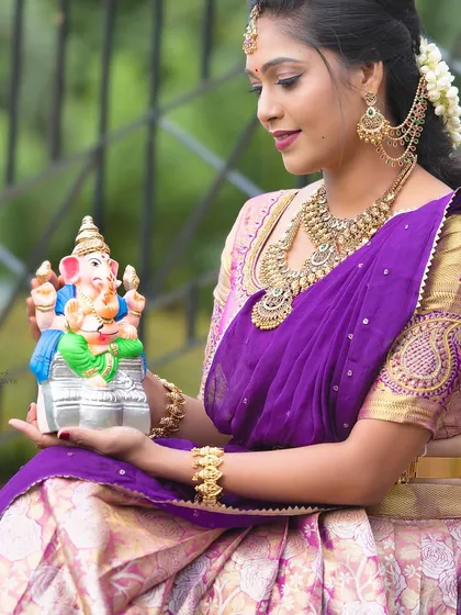 A model celebrating Ganesh Chaturthi, holding a Ganesha idol and adorned in a full temple jewellery set.