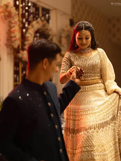 A groom gently leads his bride, a classic, romantic gesture captured during their Sangeet. The soft lighting and their elegant attire make this a timeless couple's portrait.