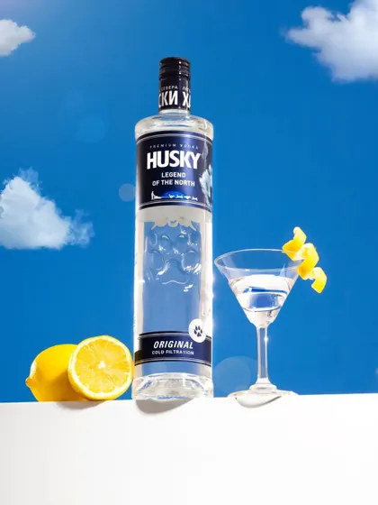 This vibrant shot for Husky Vodka uses a bright blue sky backdrop to create a feeling of freshness and open space. The composition with fresh lemons and a classic martini glass makes the product feel both premium and refreshing.