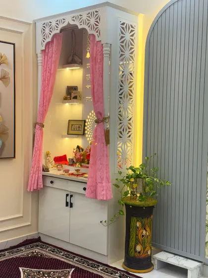 A close-up of the pooja unit, showing the intricate jali work on the doors and sides. The warm interior lighting creates a serene glow.