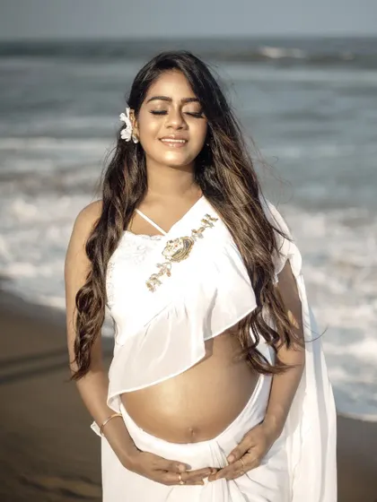 A serene, sun-kissed portrait of a mom-to-be in the white frill saree, featuring the custom mother and baby Aari work on the blouse.
