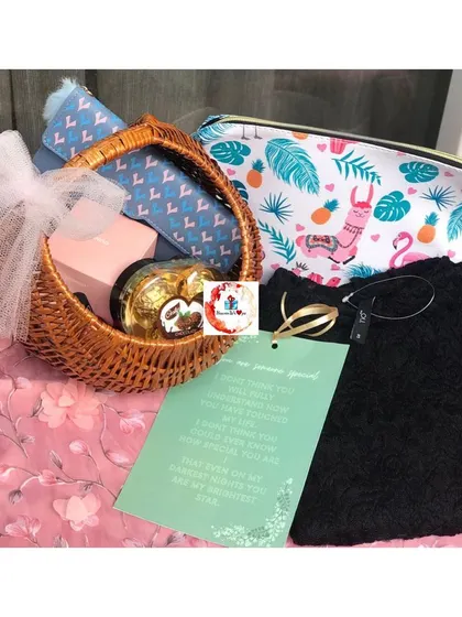 A simple yet thoughtful hamper for her, containing a small basket with Ferrero Rocher, a cosmetic pouch, a clothing item, and a personal note.