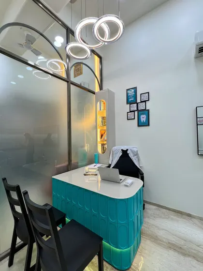 The doctor's consultation desk, featuring a vibrant teal base and a modern ring chandelier. This area is designed to be approachable and professional, with integrated storage and a clean, glossy tabletop for a clutter-free workspace.