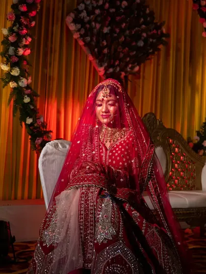 A serene portrait of the bride seated on the wedding stage, her red veil creating a beautiful frame.