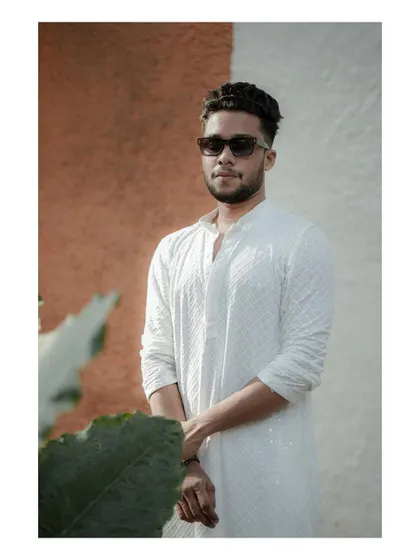 A stylish portrait of the groom against a modern, color-blocked wall, his sunglasses adding a touch of cool to his traditional outfit.