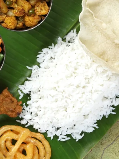 A close-up of our traditional meal, featuring fluffy rice, crisp papadum, sweet jalebi, and savoury vegetables. This is comfort food elevated for a celebration.