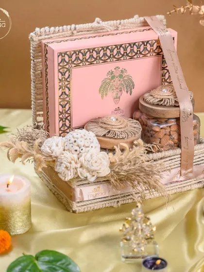 This tiered Karwa Chauth hamper is curated with a beautiful pink mithai box and jars of nuts, all arranged in a rustic basket. It's a perfect blend of tradition and luxury.