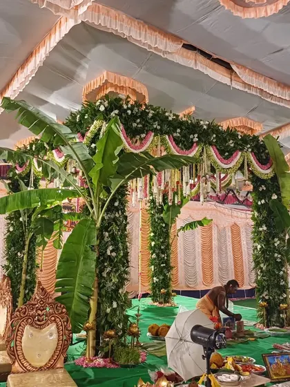A priest preparing for a ceremony at a traditional South Indian mandap, decorated with banana plants and floral garlands.