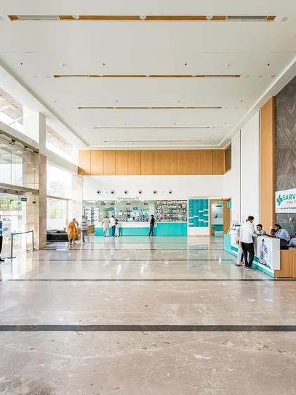 Another view of the Sarvesh Health City lobby, showcasing the clean marble floors, wood accents, and organized reception desks. The design ensures a smooth and stress-free experience for patients and visitors from the moment they arrive.