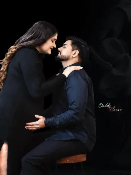 An intimate portrait of a couple dressed in black. The dark, moody lighting creates a romantic and sophisticated atmosphere for this studio maternity session.