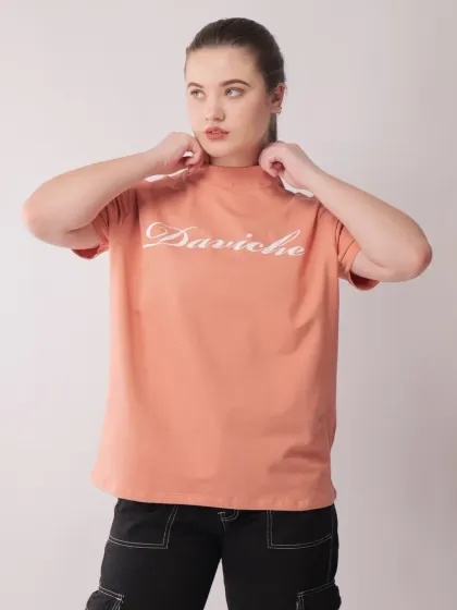 A model adjusting the collar of a peach-colored t-shirt, a simple action that adds a natural and unposed feel to the photograph.