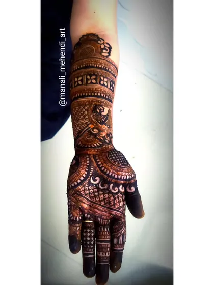 An intricate mehandi design covering the hand and forearm. This piece combines floral, peacock, and geometric patterns, typical of traditional bridal mehandi.