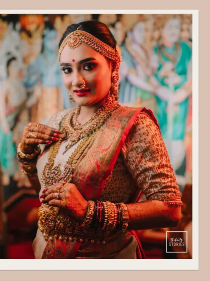A classic portrait of a South Indian bride in all her glory, adorned with layers of traditional gold jewelry and a beautiful silk saree.