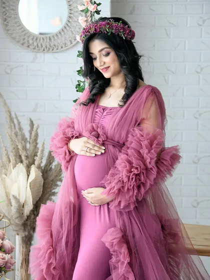 A close-up solo portrait highlighting the beautiful details of the dusty rose ruffled gown and the mom-to-be's serene expression. The boho backdrop adds a touch of warmth.