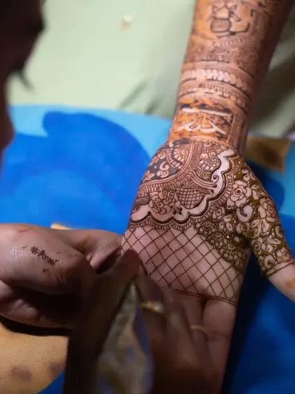 A detailed macro shot of the henna cone applying the intricate patterns onto the bride's hand.