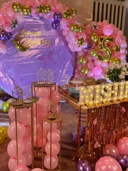 A glamorous pink and purple 5th birthday party for Mishika. The room is filled with metallic balloons, a large backdrop, multiple pedestals for treats, and light-up letters for the name.