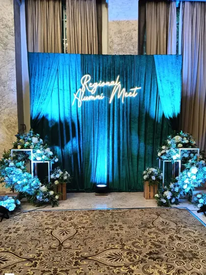 For this regional alumni meet, I designed a sophisticated stage with a rich green velvet curtain and a custom neon sign. The blue uplighting and floral arrangements create a premium and memorable atmosphere for formal gatherings.