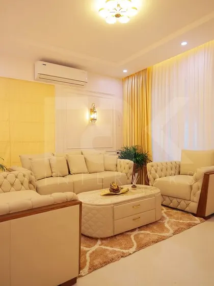A luxurious living room featuring classic design elements like tufted sofas and wall molding. The warm yellow and cream color palette, combined with elegant lighting, creates a grand and inviting atmosphere.