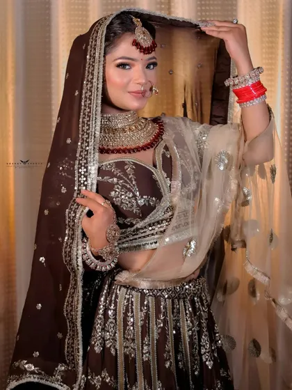 A full-length portrait of the bride holding her veil. The brown and gold sequined lehenga shimmers in the light, showcasing its intricate craftsmanship.